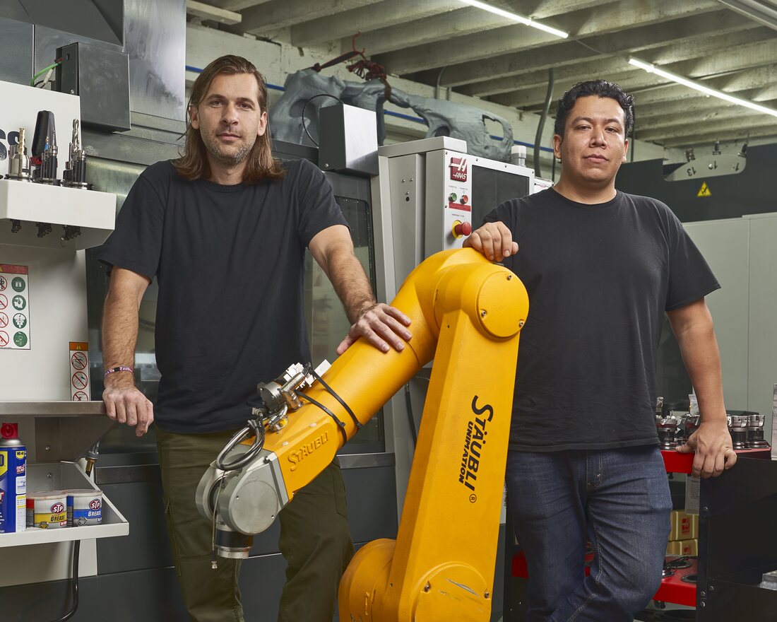Wil Barnes and Oscar Elizalde on the shop floor beside a robot arm in Brooklyn, NY